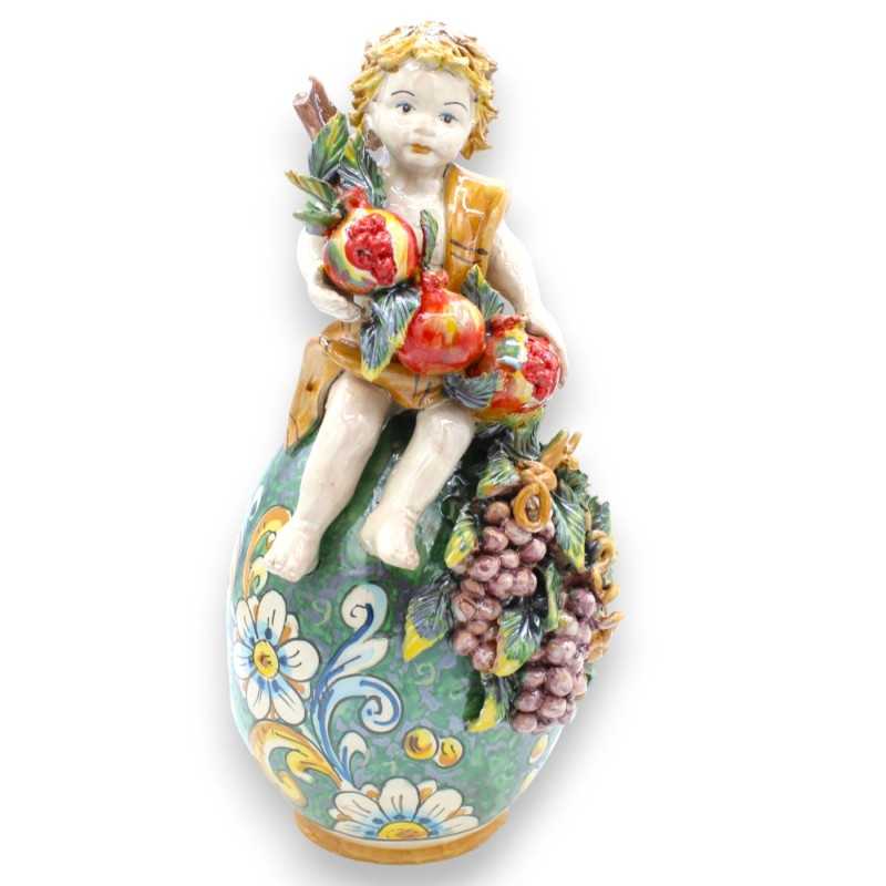 Putto on egg with bunch of pomegranates and grapes, Caltagirone ceramic - h 33 cm approx. verdigris, Baroque and flowers